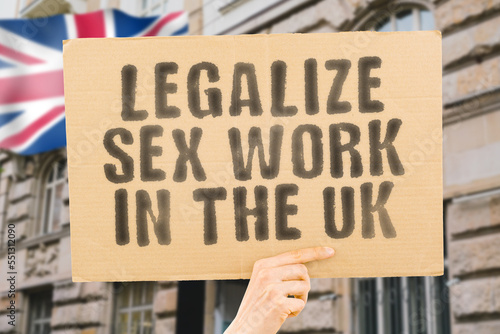 The phrase " Legalize Sex Work in the UK " is on a banner in men's hands with blurred background. Guide. Govern. Body. Coworker. Crime. Criminal. Democracy. Desire. Employee. Earnings. Dollars © AndriiKoval