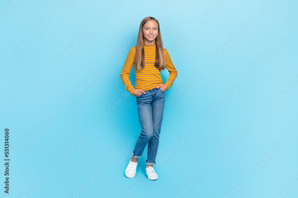 Full size photo of optimistic small girl with straight hairdo wear yellow pullover hands in pockets isolated on blue color background Full size photo of optimistic small girl with straight hairdo wear yellow pullover hands in pockets isolated on blue color background