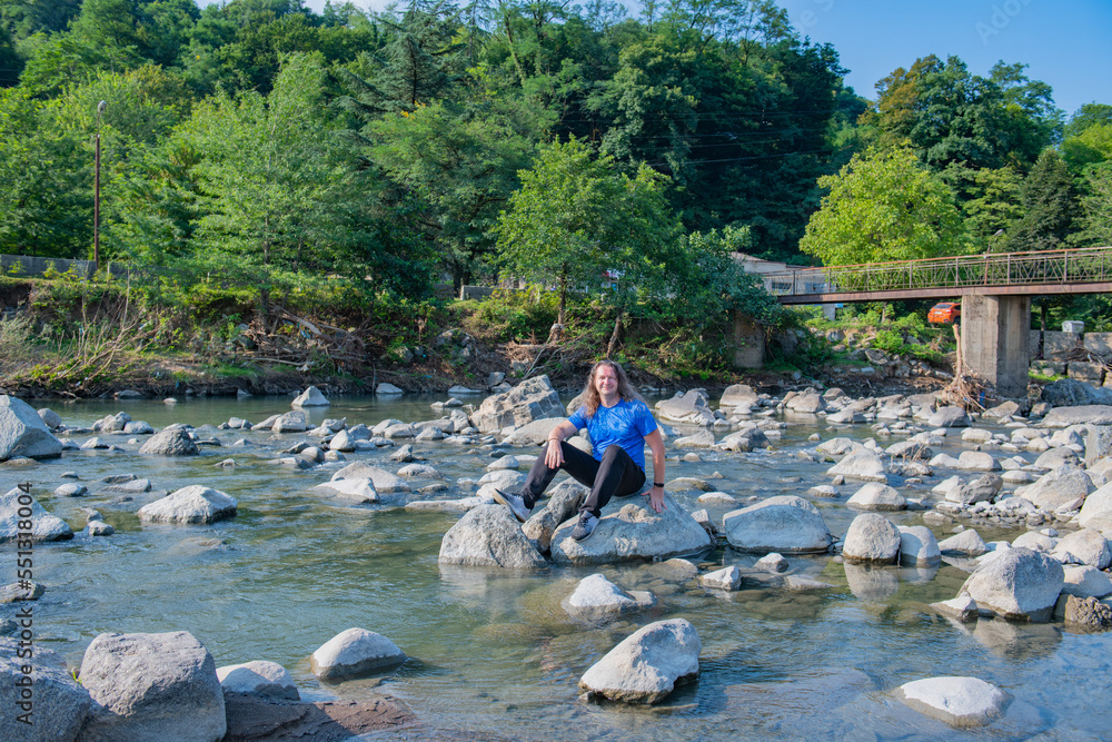 In blue clothes, a man sits on a stone by the river