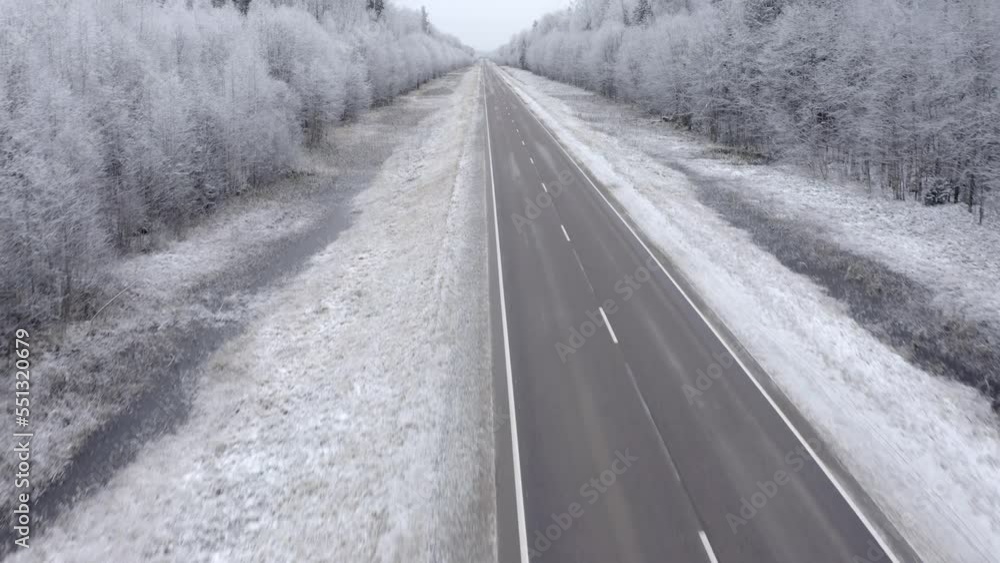 Flying forward straight over the road without cars in the forest covered with snow Flying forward straight over the road without cars in the forest covered with snow