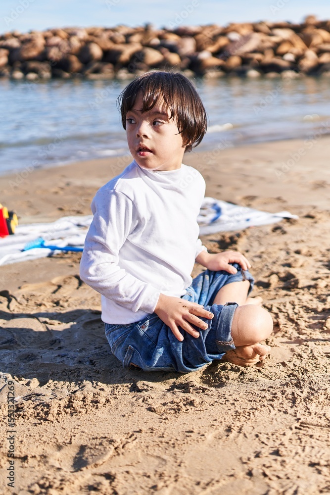 Down syndrome kid playing with relaxed expression sitting on sand at beach Down syndrome kid playing with relaxed expression sitting on sand at beach