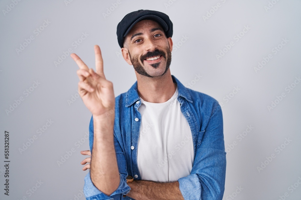 Hispanic man with beard standing over isolated background smiling with happy face winking at the camera doing victory sign with fingers. number two. Hispanic man with beard standing over isolated background smiling with happy face winking at the camera doing victory sign with fingers. number two.