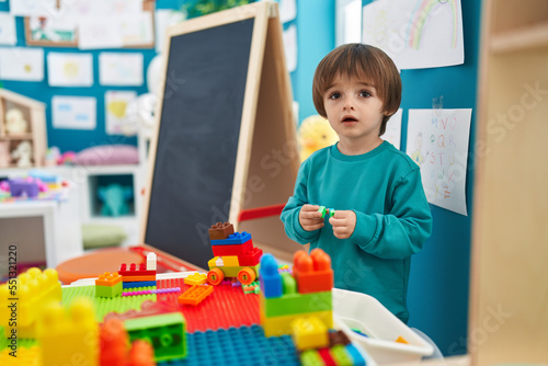 Adorable toddler playing with construction blocks standing at kindergarten