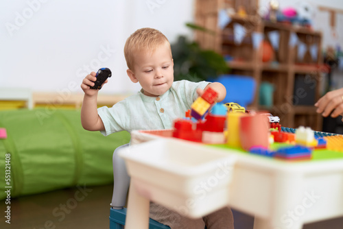 Adorable toddler playing with construction blocks holding car at kindergarten