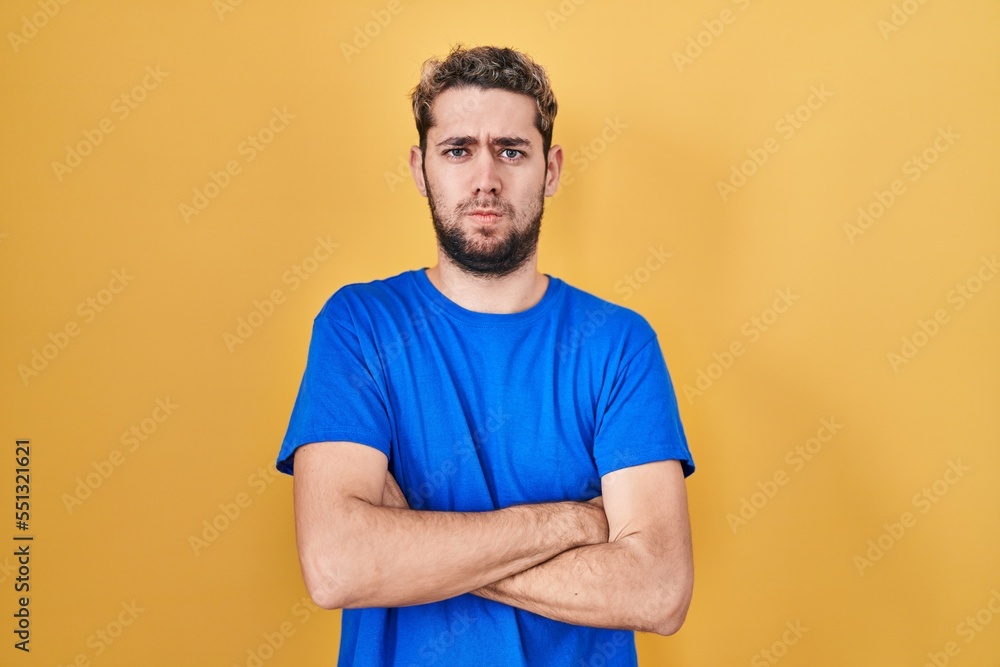 Hispanic man with beard standing over yellow background skeptic and nervous, disapproving expression on face with crossed arms. negative person. Hispanic man with beard standing over yellow background skeptic and nervous, disapproving expression on face with crossed arms. negative person.
