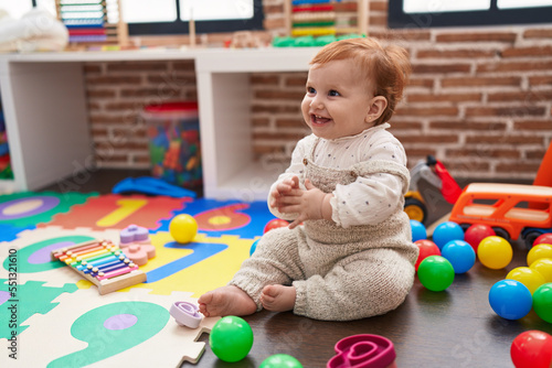 Adorable redhead toddler sitting on floor applauding at kindergarten