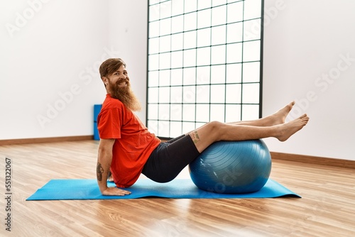 Young redhead man smiling confident training using fit ball at sport center