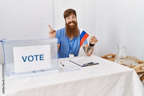 Caucasian man with long beard at political campaign election holding russia flag smiling happy pointing with hand and finger to the side