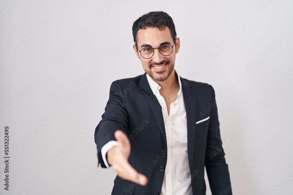 Handsome business hispanic man standing over white background smiling friendly offering handshake as greeting and welcoming. successful business. Handsome business hispanic man standing over white background smiling friendly offering handshake as greeting and welcoming. successful business.