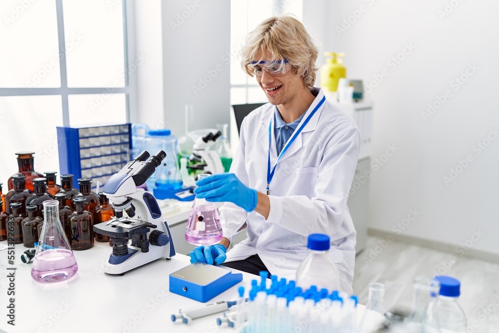 Fototapeta premium Young blond man scientist smiling confident weighing test tube at laboratory