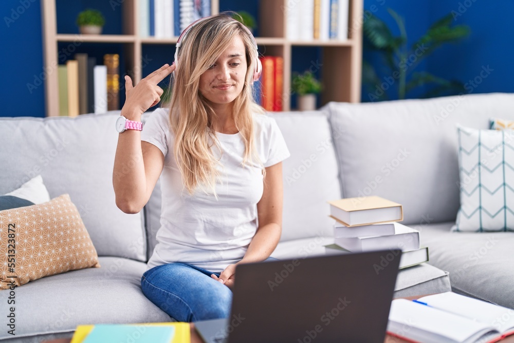 Young blonde woman studying using computer laptop at home shooting and killing oneself pointing hand and fingers to head like gun, suicide gesture. Young blonde woman studying using computer laptop at home shooting and killing oneself pointing hand and fingers to head like gun, suicide gesture.