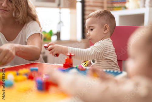 Teacher and preschool student playing with car toy sitting on table at kindergarten