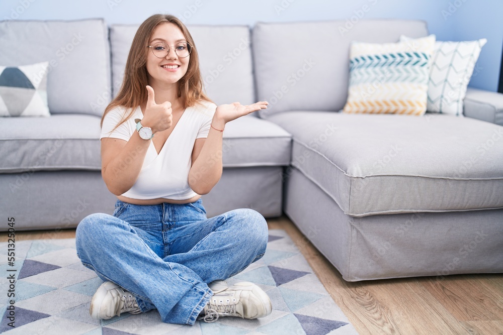 Young caucasian woman sitting on the floor at the living room showing palm hand and doing ok gesture with thumbs up, smiling happy and cheerful Young caucasian woman sitting on the floor at the living room showing palm hand and doing ok gesture with thumbs up, smiling happy and cheerful