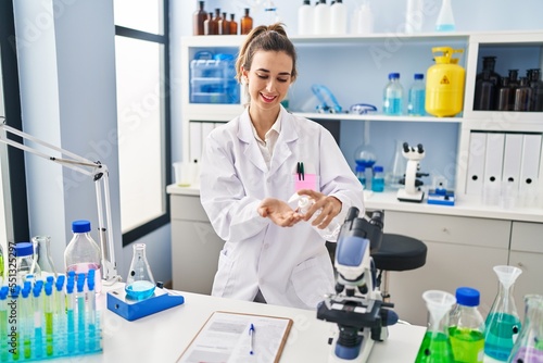 Young woman wearing scientist uniform using sanitizer hands gel at laboratory
