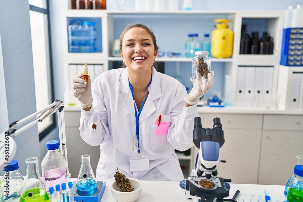 Young hispanic woman doing weed oil extraction at laboratory smiling and laughing hard out loud because funny crazy joke. Young hispanic woman doing weed oil extraction at laboratory smiling and laughing hard out loud because funny crazy joke.