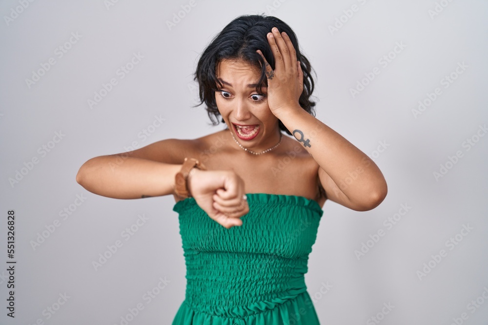 Young hispanic woman standing over isolated background looking at the watch time worried, afraid of getting late Young hispanic woman standing over isolated background looking at the watch time worried, afraid of getting late