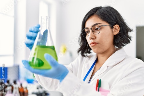 Fototapeta Naklejka Na Ścianę i Meble -  Young latin woman wearing scientist uniform measuring liquid on test tube at laboratory