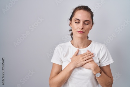 Beautiful brunette woman standing over isolated background smiling with hands on chest with closed eyes and grateful gesture on face. health concept.