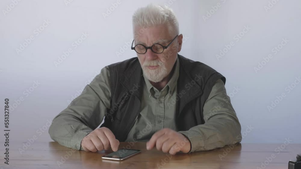 Caucasian sad elderly man searches for information on smartphone without finding it Caucasian sad elderly man searches for information on smartphone without finding it