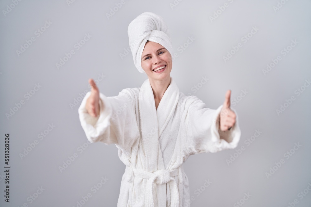 Blonde caucasian woman wearing bathrobe looking at the camera smiling with open arms for hug. cheerful expression embracing happiness. Blonde caucasian woman wearing bathrobe looking at the camera smiling with open arms for hug. cheerful expression embracing happiness.