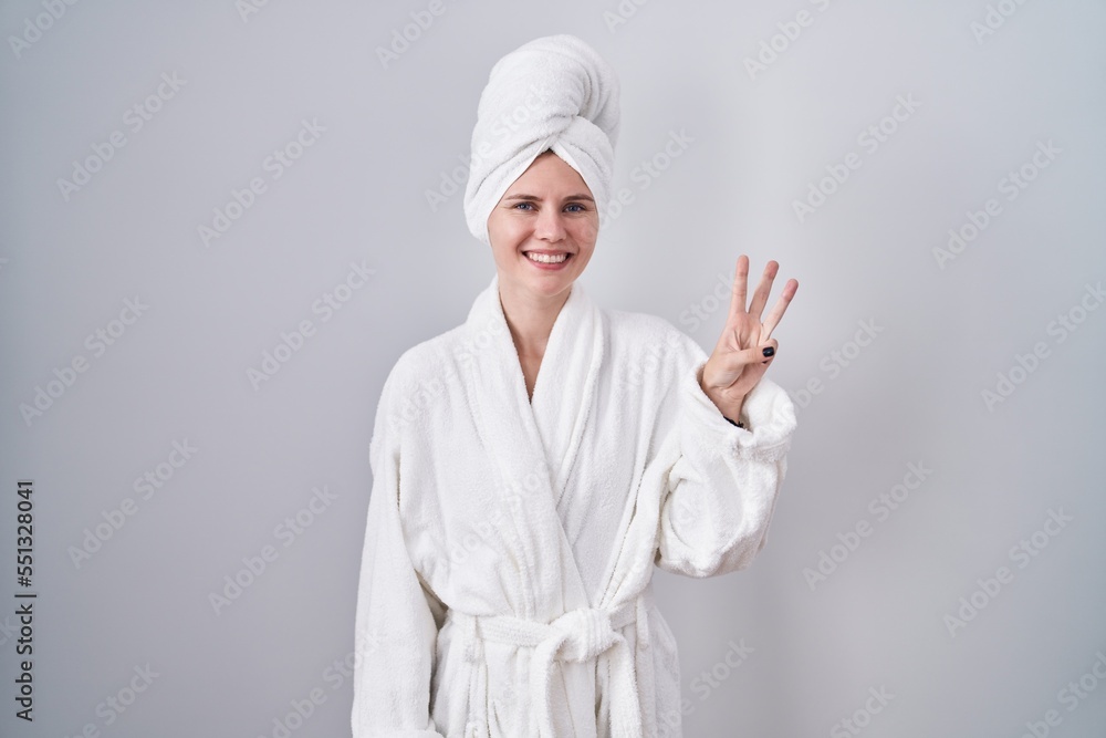 Blonde caucasian woman wearing bathrobe showing and pointing up with fingers number three while smiling confident and happy. Blonde caucasian woman wearing bathrobe showing and pointing up with fingers number three while smiling confident and happy.