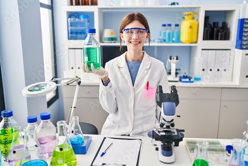 Young brunette woman working at scientist laboratory looking positive and happy standing and smiling with a confident smile showing teeth