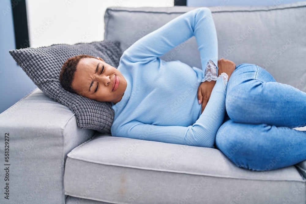 African american woman suffering for menstrual pain lying on sofa at home African american woman suffering for menstrual pain lying on sofa at home