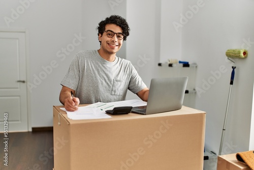 Young hispanic man calculate economy using laptop at new home.
