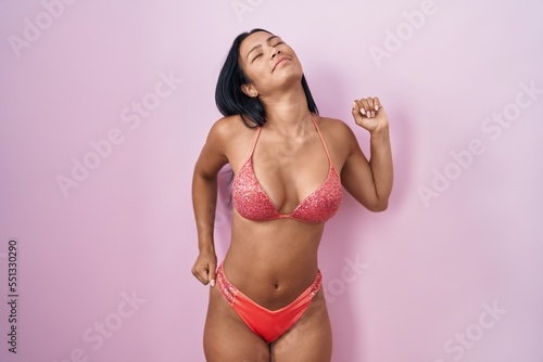 Hispanic woman wearing bikini stretching back, tired and relaxed, sleepy and yawning for early morning