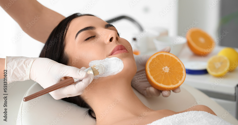 Cosmetologist applying mask with vitamin C onto woman's face in beauty salon Cosmetologist applying mask with vitamin C onto woman's face in beauty salon