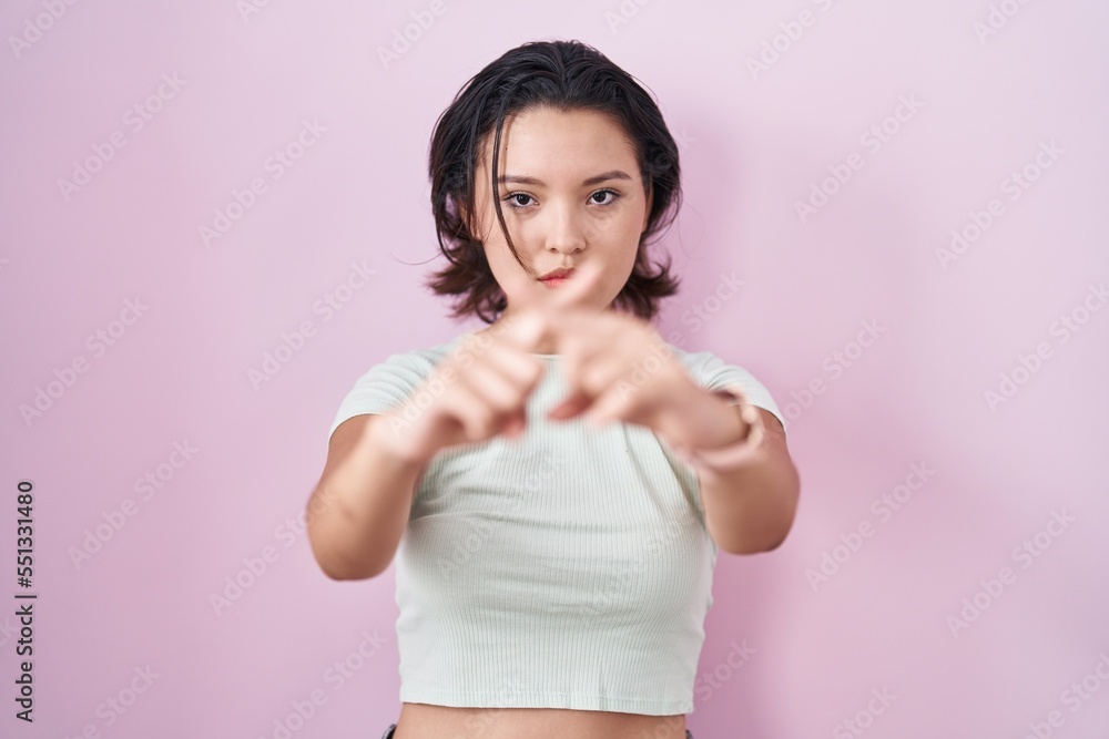Hispanic young woman standing over pink background rejection expression crossing fingers doing negative sign Hispanic young woman standing over pink background rejection expression crossing fingers doing negative sign