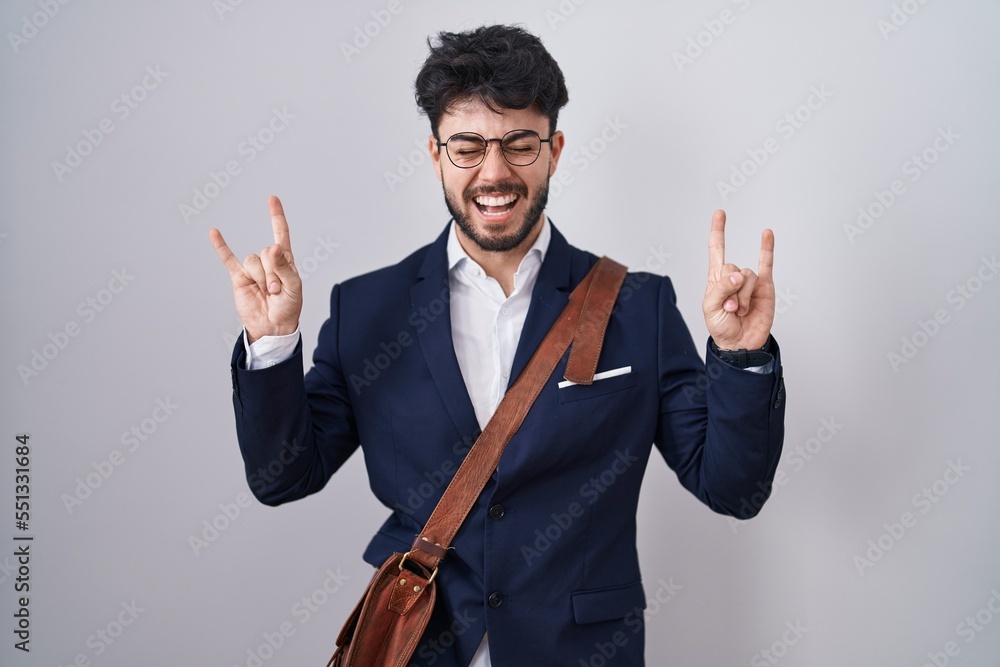 Hispanic man with beard wearing business clothes shouting with crazy expression doing rock symbol with hands up. music star. heavy music concept. Hispanic man with beard wearing business clothes shouting with crazy expression doing rock symbol with hands up. music star. heavy music concept.