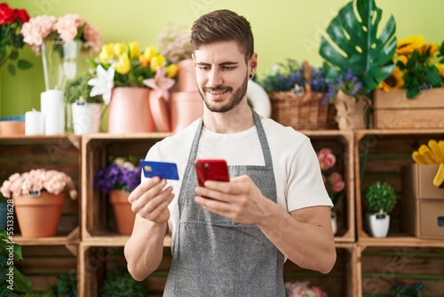 Young caucasian man florist using smartphone and credit card at flower shop