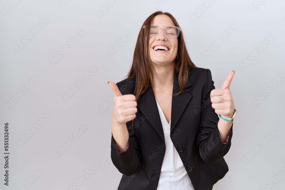Beautiful brunette woman wearing business jacket and glasses success sign doing positive gesture with hand, thumbs up smiling and happy. cheerful expression and winner gesture. Beautiful brunette woman wearing business jacket and glasses success sign doing positive gesture with hand, thumbs up smiling and happy. cheerful expression and winner gesture.