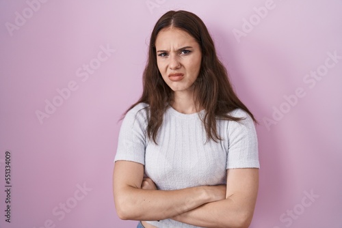 Young hispanic girl standing over pink background skeptic and nervous, disapproving expression on face with crossed arms. negative person.