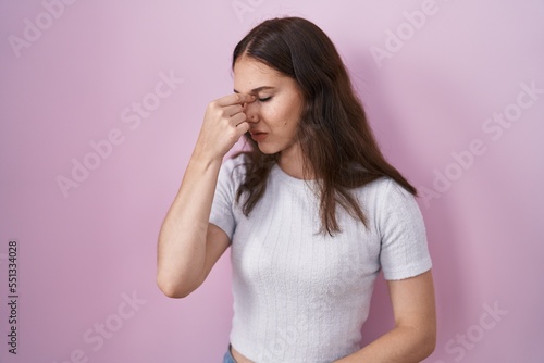 Young hispanic girl standing over pink background tired rubbing nose and eyes feeling fatigue and headache. stress and frustration concept.