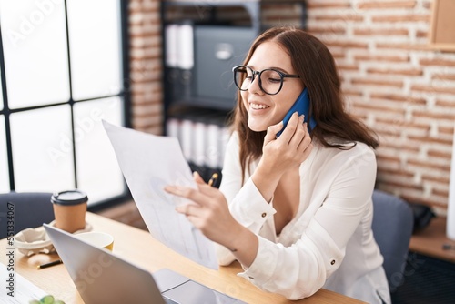 Young woman business worker talking on smartphone reading document at office