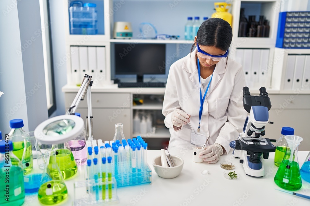 Fototapeta premium Young latin woman wearing scientist uniform using pipette at laboratory