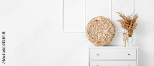 Interior of room with chest of drawers and reeds in vase near white wall with space for text