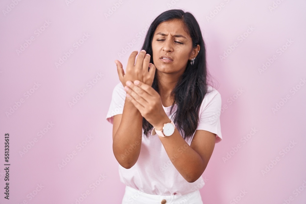 Young hispanic woman standing over pink background suffering pain on hands and fingers, arthritis inflammation Young hispanic woman standing over pink background suffering pain on hands and fingers, arthritis inflammation