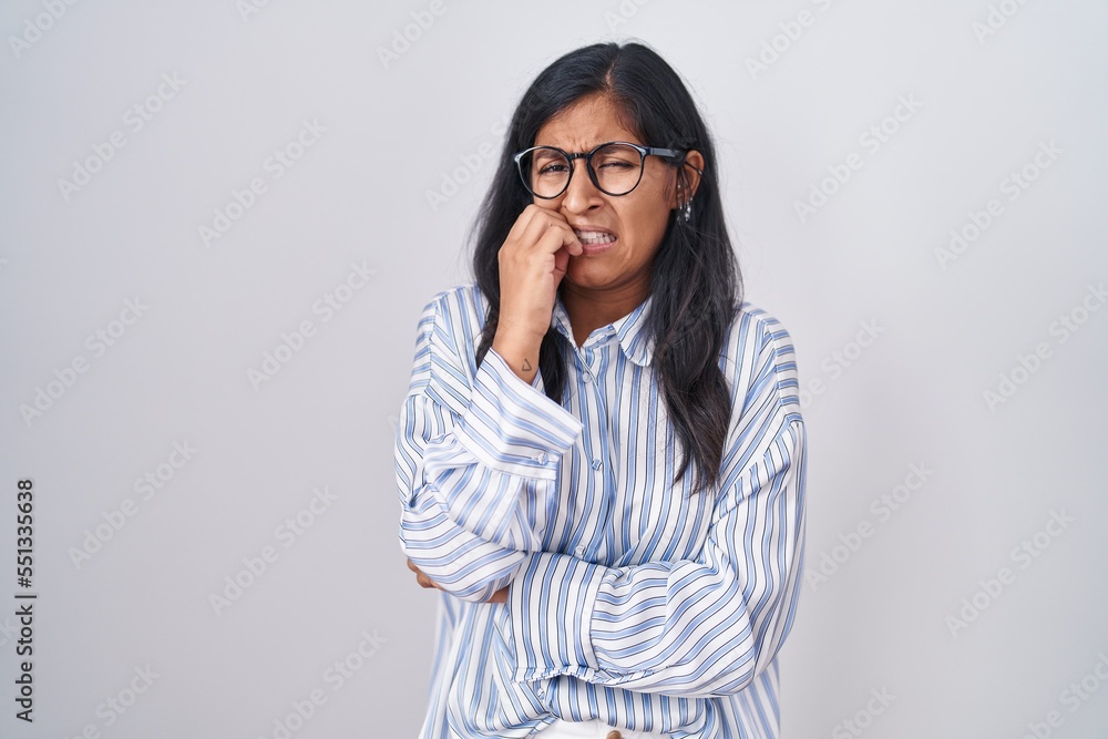 Young hispanic woman wearing glasses looking stressed and nervous with hands on mouth biting nails. anxiety problem. Young hispanic woman wearing glasses looking stressed and nervous with hands on mouth biting nails. anxiety problem.