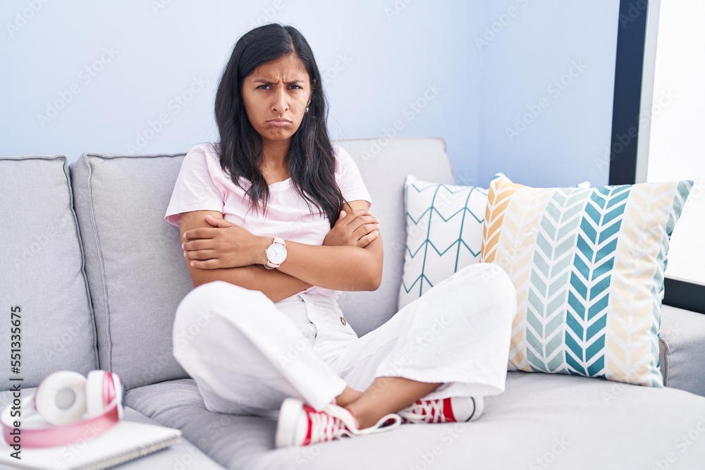 Young hispanic woman sitting on the sofa at home skeptic and nervous, disapproving expression on face with crossed arms. negative person. Young hispanic woman sitting on the sofa at home skeptic and nervous, disapproving expression on face with crossed arms. negative person.