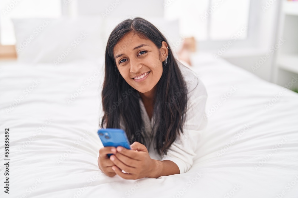 Young beautiful hispanic woman using smartphone lying on bed at bedroom Young beautiful hispanic woman using smartphone lying on bed at bedroom