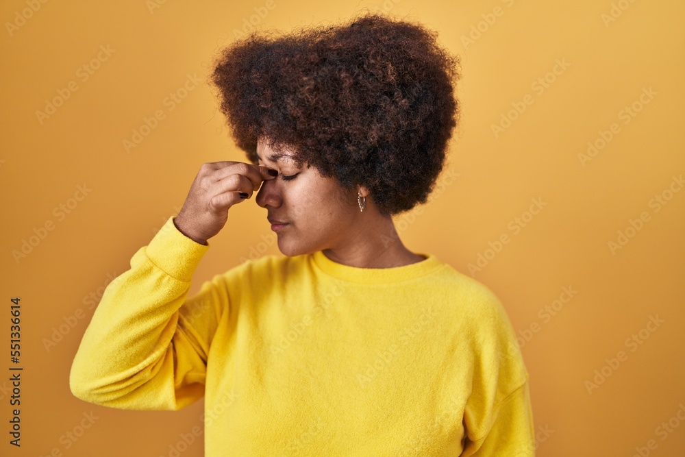 Young african american woman standing over yellow background tired rubbing nose and eyes feeling fatigue and headache. stress and frustration concept. Young african american woman standing over yellow background tired rubbing nose and eyes feeling fatigue and headache. stress and frustration concept.
