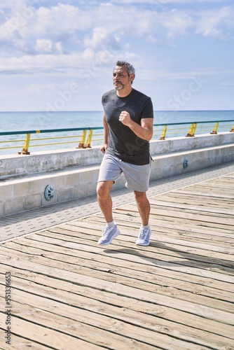 Fototapeta Naklejka Na Ścianę i Meble -  Middle age hispanic man wearing sportswear running at seaside