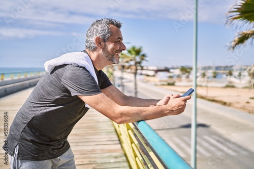 Middle age hispanic man wearing sportswear using smartphone at seaside