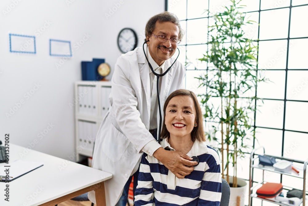 Obraz premium Middle age man and woman wearing doctor uniform having medical consultation auscultating using stethoscope at clinic