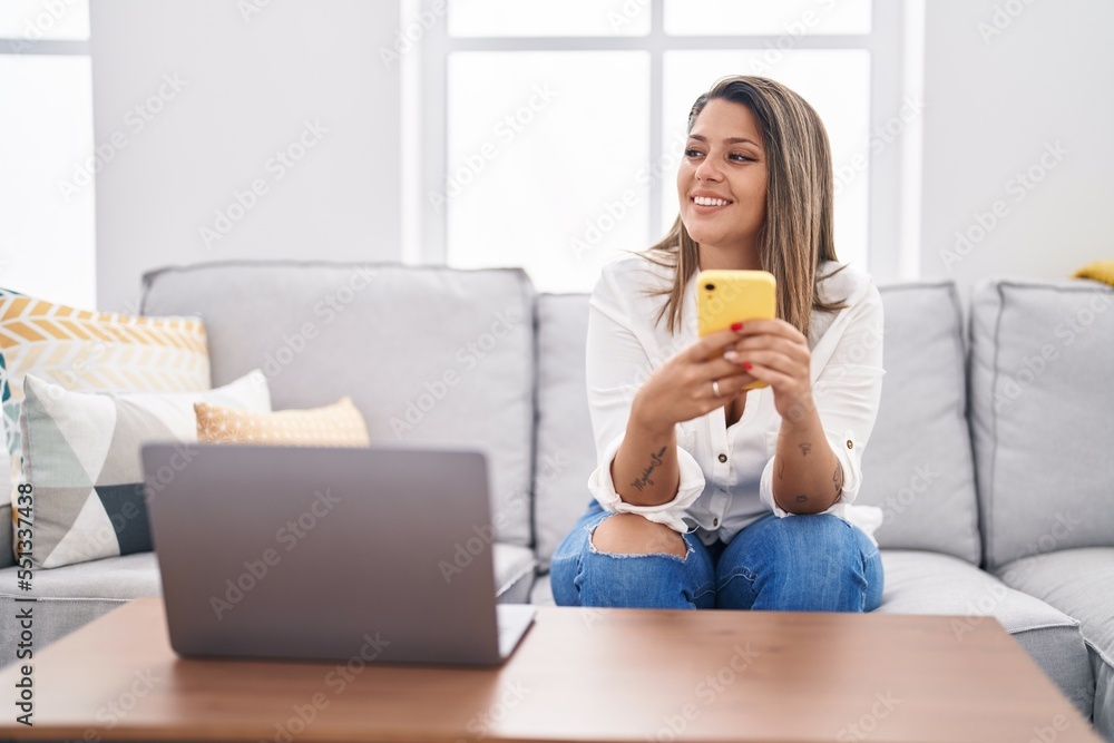 Young hispanic woman using smartphone sitting on sofa at home Young hispanic woman using smartphone sitting on sofa at home