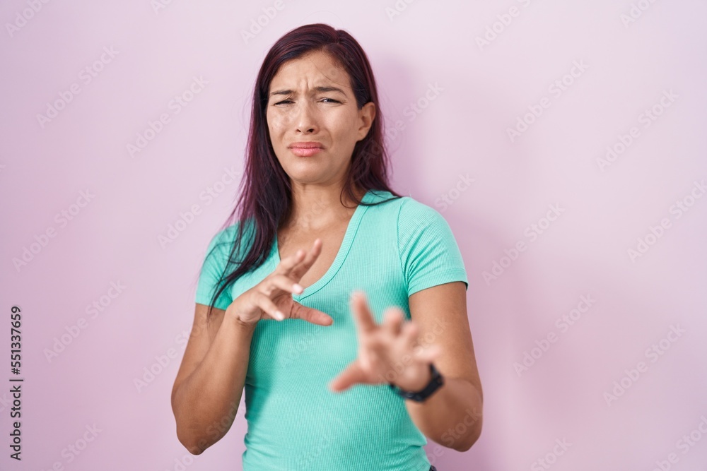 Young hispanic woman standing over pink background disgusted expression, displeased and fearful doing disgust face because aversion reaction. Young hispanic woman standing over pink background disgusted expression, displeased and fearful doing disgust face because aversion reaction.