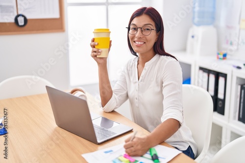 Young beautiful hispanic woman business worker writing document drinking coffee at office